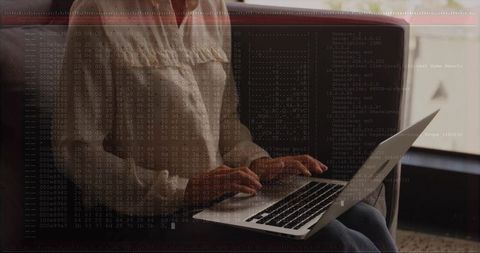 Typing woman wearing blouse and jeans on couch by window with laptop and code overlay