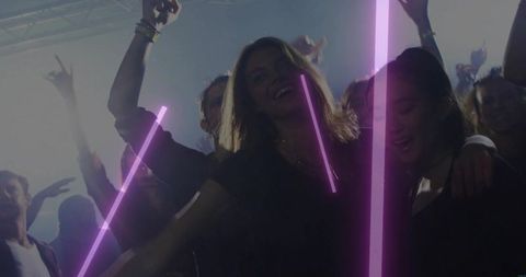 Smiling women dancing under purple neon beams on crowded nightclub dancefloor