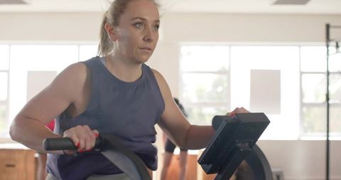 Determined woman pedaling stationary bike in bright gym studio with digital console