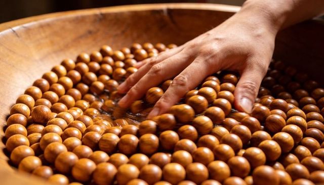 Right hand sliding over polished wooden beads in carved bowl for texture and calm