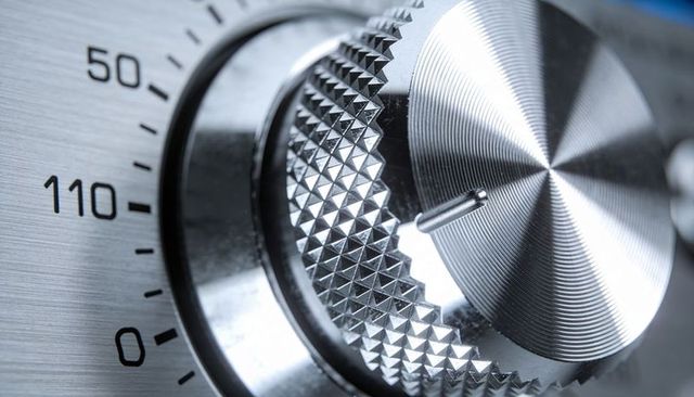 Macro knurled metal control knob rotating on brushed steel dial with scale and pointer
