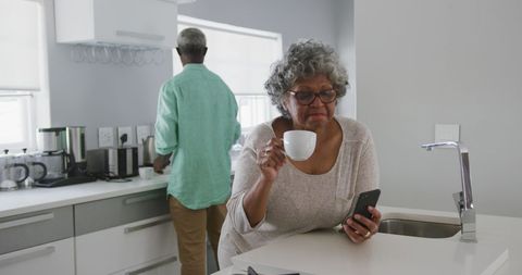 Senior Woman Enjoying Coffee and Checking Phone in Modern Kitchen