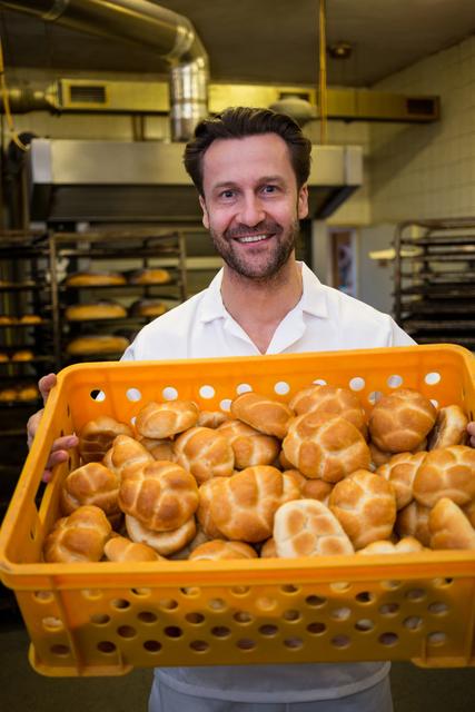 Baker holding a basket filled with freshly baked buns, smiling proudly in a commercial kitchen. Ideal for use in advertisements for bakeries, culinary schools, food blogs, and small business promotions. Highlights the joy and satisfaction of baking and the quality of homemade bread.