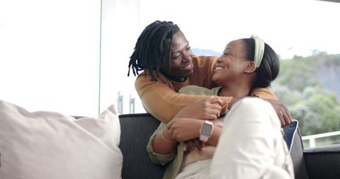 African American Couple Embracing on Sofa, Smiling and Relaxing in Sunlit Living Room