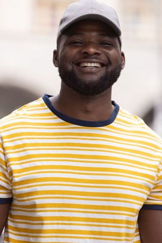 Confident african man smiling in yellow striped tee and gray cap urban headshot