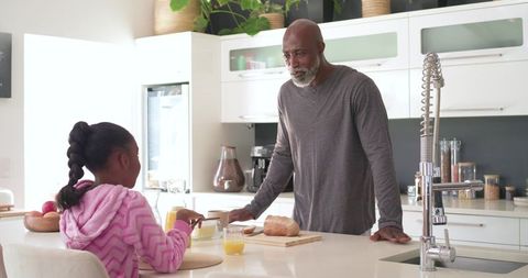African american father and daughter preparing breakfast together in bright modern kitchen