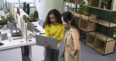 Diverse female colleagues working on laptop in modern office