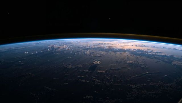 Low orbit dawn over earth showing curved horizon, terminator shadows and atmospheric airglow