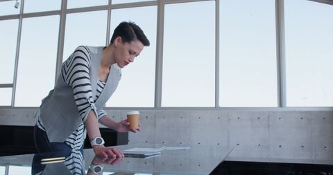 Focused Businesswoman Reviewing Documents with Coffee in Hand