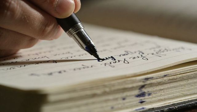 Writing with fountain pen on journal, close-up nib and ink blot capturing craftsmanship