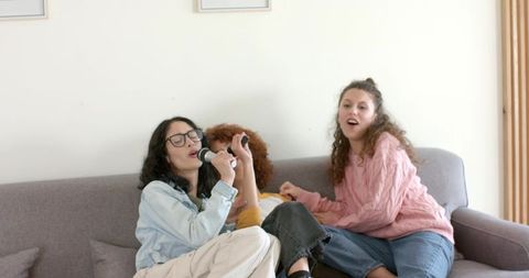 Friends singing karaoke on couch: cozy living room party with microphone and laughter