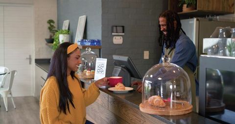 Indian woman smiling while ordering coffee and croissant at modern cafe counter