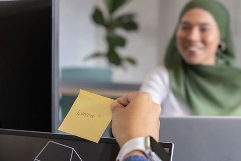 Passing lunch note between coworkers wearing hijab in modern office workspace