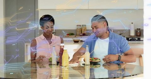Couple reaching for condiments at kitchen table with futuristic circuit-style overlay