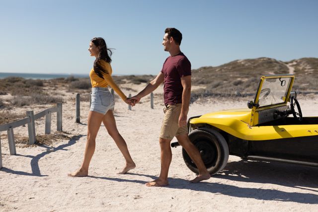 This image shows a happy couple holding hands and walking away from a beach buggy on a sunny beach. Ideal for use in travel brochures, romantic getaway promotions, summer holiday advertisements, and lifestyle blogs focusing on adventure and outdoor activities.