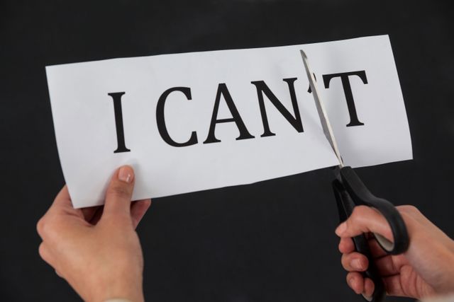 Businesswoman cutting paper with the words 'I CAN'T' to create 'I CAN', symbolizing motivation and positive change. Ideal for use in motivational posters, self-improvement blogs, business presentations, and educational materials promoting a growth mindset and empowerment.