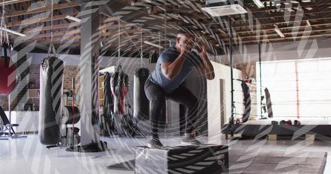 Landing box jump on padded box in industrial gym with punching bags and daylight