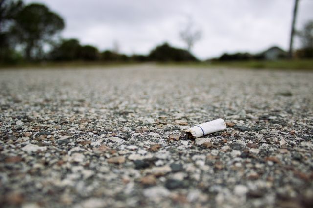 Discarded cigarette butt lies on rural asphalt road, highlighting pollution and littering issues. Useful for campaigns on environmental protection, public awareness on pollution, and educational materials focused on outdoor stability.