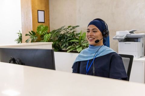 Smiling hijab-wearing receptionist answering calls at modern office reception desk