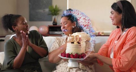 Woman receiving surprise 30th birthday cake while holding baby on sofa
