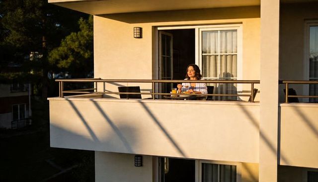 Sunlit balcony breakfast with woman holding orange juice on urban terrace, relaxation