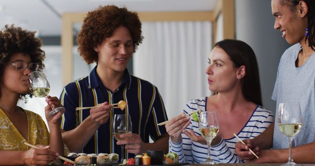 This image depicts a joyful group of multiracial friends dining together and enjoying sushi and wine. They are engaged in conversation and laughter, creating a warm and social atmosphere. Ideal for themes on friendship, multicultural gatherings, dining experiences, and lifestyle articles or advertisements promoting food, beverages, and social events.