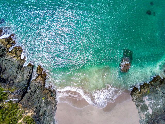 Stunning bird's eye view of crystal-clear turquoise waters gently lapping against a rocky shoreline with white sandy beach. Perfect for travel magazines, beach resort advertisements, or nature blogs emphasizing scenic views and coastal beauty.