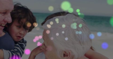 Grandparents embracing grandchildren on beach shoreline with warm bokeh light effects