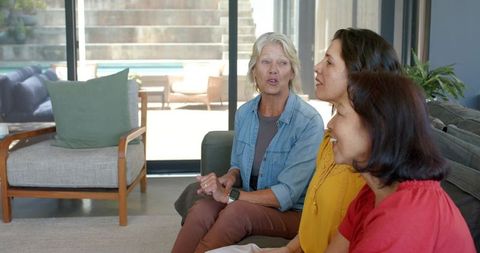 Three women chatting and laughing on sofa, multigenerational friends enjoying conversation