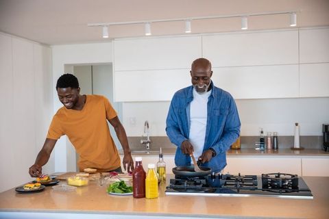 Father and son spending quality time cooking together in sleek modern kitchen. Bright space shows joy of culinary skill and family bonding. Ideal for uses related to family dynamics, culinary experiences, positive home life, and highlighting modern interior designs.