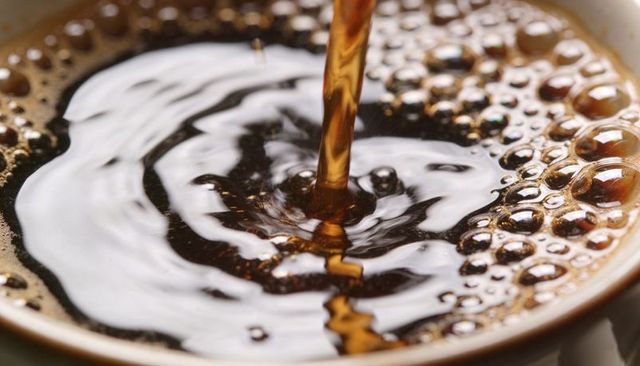 Pouring dark coffee creating concentric ripples and frothy crema in ceramic cup