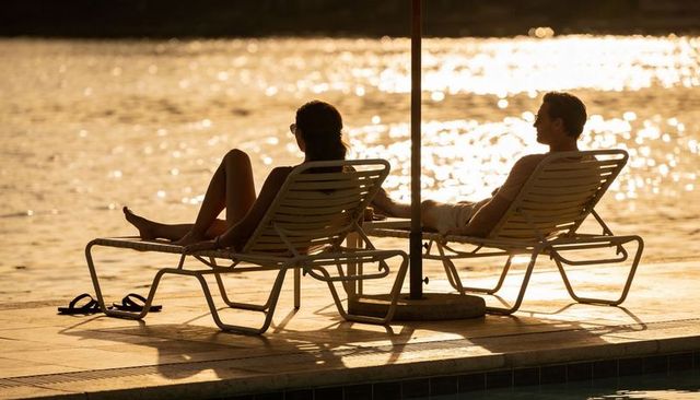 Couple relaxing on lakefront loungers at golden sunset silhouettes and warm reflections