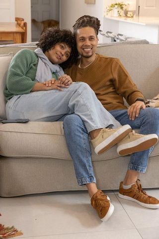 Couple cuddling on grey sofa in cozy modern living room, smiling and relaxing, enjoying quiet moment