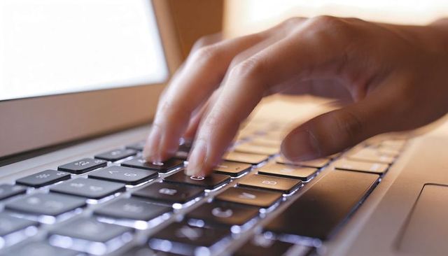 Close-up hands typing on backlit laptop keyboard, low-light workspace productivity