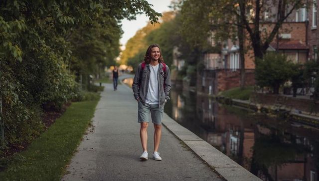 Young man walking along canal path with backpack in casual summer outfit