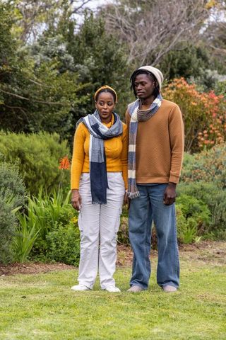African american couple standing in garden wearing knit sweaters scarves