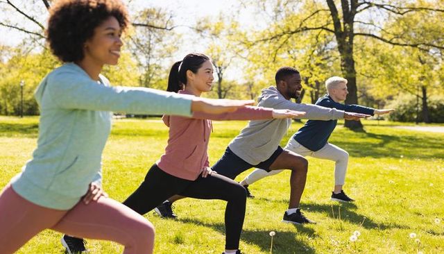 Diverse group practicing lunges on green lawn during sunny spring outdoor fitness session