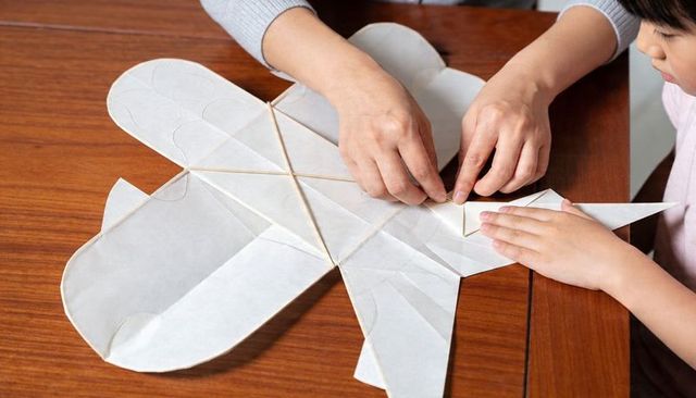 Parent and child assembling paper kite on wooden table, hands-on family craft activity