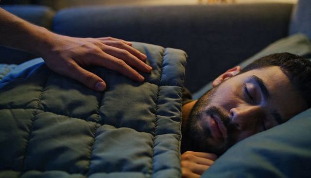 Partner placing hand on sleeping man under quilted comforter on couch at night