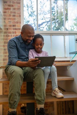 African american father and daughter sharing tablet and learning together on wooden stairs