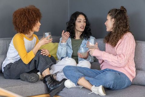 Diverse friends chatting on sofa, holding drinks, cozy casual home conversation