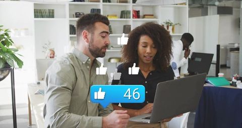 Colleagues boosting social engagement on laptop with animated like icons in modern office