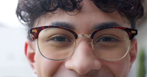 Young man wearing tortoiseshell round glasses with gold bridge smiling close-up headshot