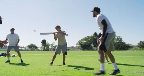 Diverse friends playing cricket in park on sunny day, batting and fielding for amateur team fun
