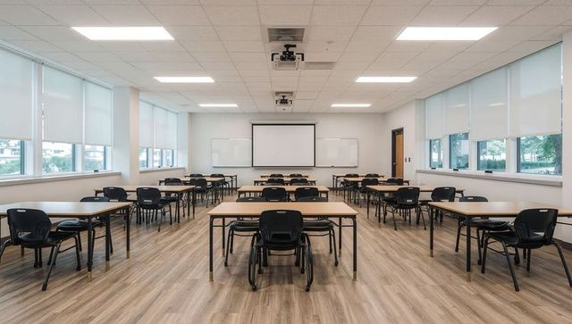 Modern classroom featuring rows of desks, black chairs, projector screen, natural light