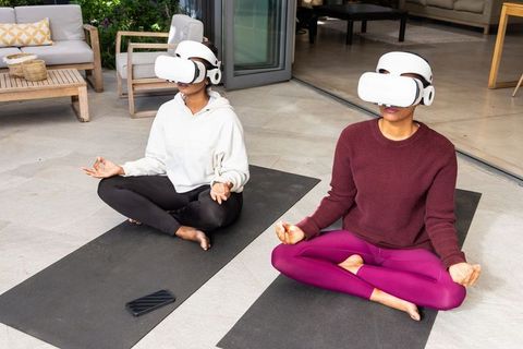 African american and indian women meditating with vr headsets on patio yoga mats