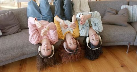 Upside-down teenage friends listening to music on sofa with colorful over-ear headphones