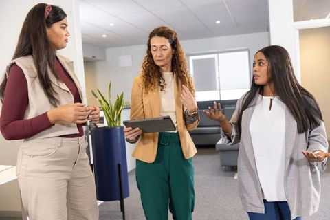 Diverse women collaborating around tablet in modern office lounge for teamwork and leadership