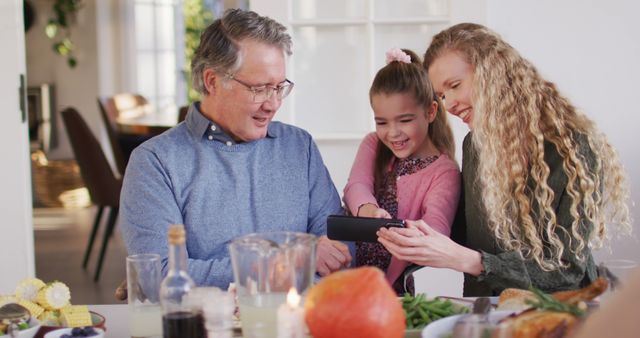 Image of happy caucasian mother, daughter and grandfather looking at smartphone at dinner table. Family, domestic life and togetherness concept digitally generated image.