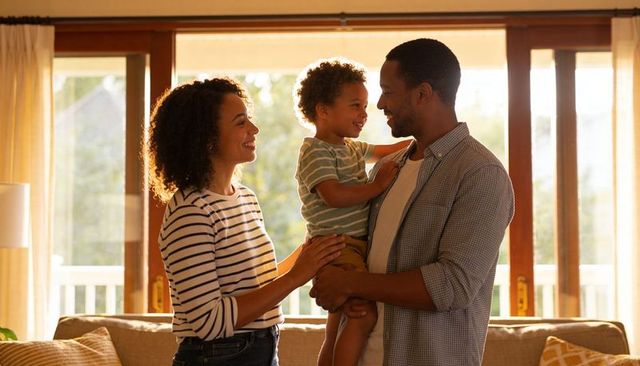 Parents holding toddler in sunlit living room, sharing warm family moment and close bond
